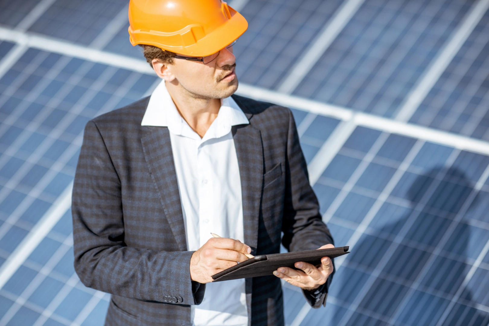 Business man in construction hat holding ipad and standing in front of solar panels