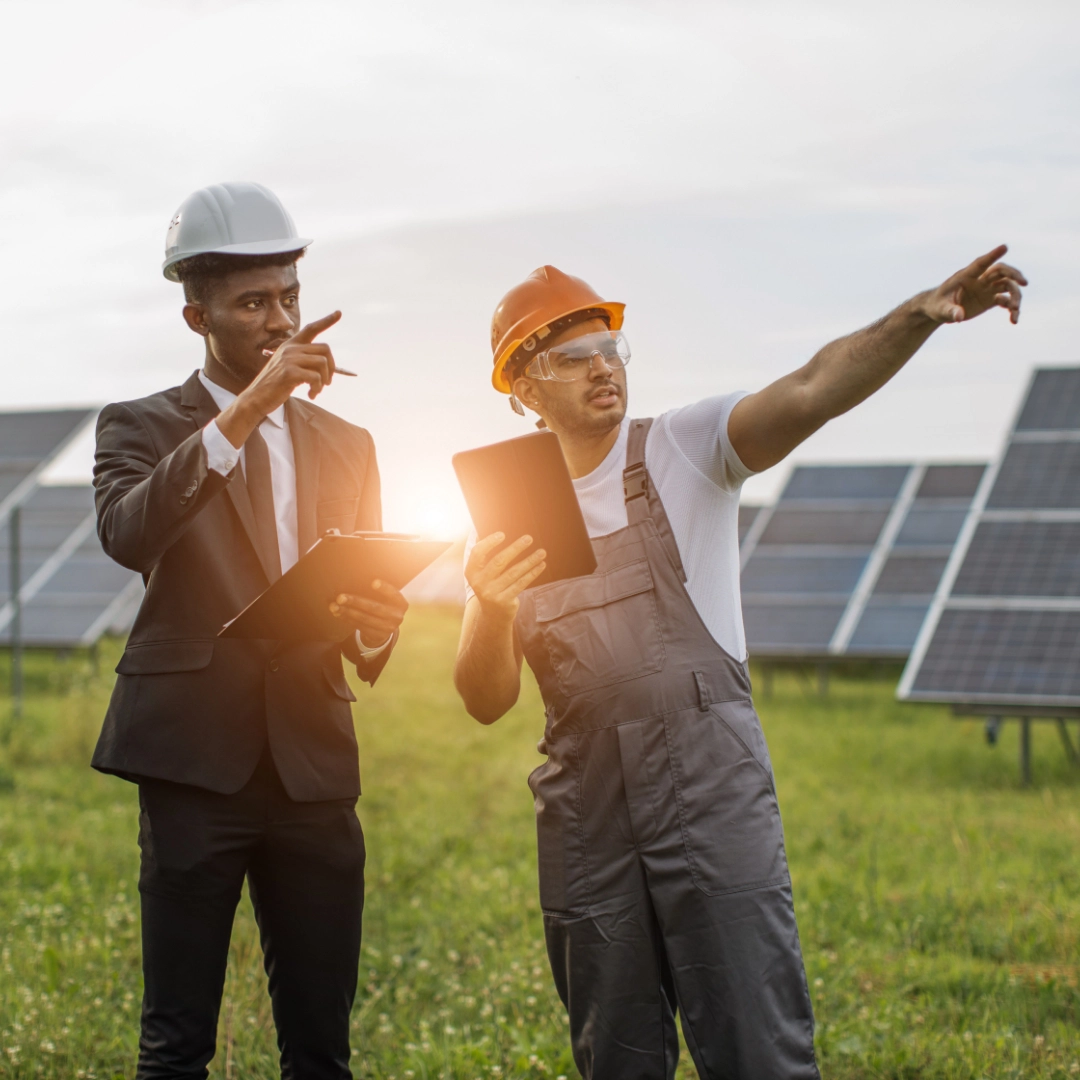 Two men in construction hats pointing toward something, with solar panels in the background
